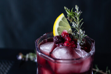 Cocktail garnish made with berries, rosemary and lemon. Close-up shot with dark background.