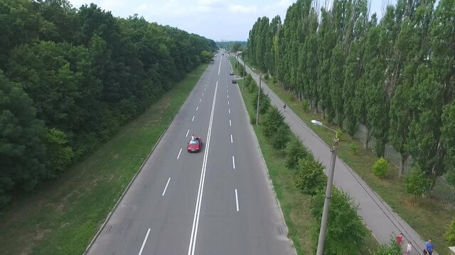 Aerial shot of red convertible car riding through empty highway. Young couple traveling at cabriolet. Happy just married pair enjoying journey. Flying over auto driving at road on summer day. Slow mo