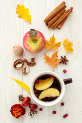 Autumn tea. A cup of tea with fallen leaves, apples and nuts on a white wooden background. 
