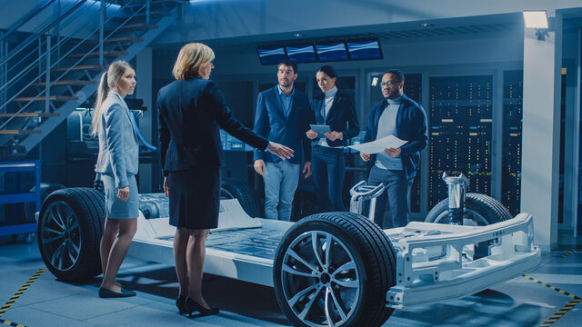 International Team of Automobile Design Engineers Introducing Futuristic Autonomous Electric Car Platform Chassis to Group of Investors and Businesspeople. Vehicle Frame with Wheels, Engine, Battery