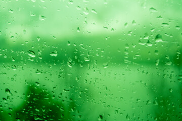 Raindrops on a window, illustrating gray and rainy weather during the day. Green background.