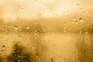 Raindrops on a window, illustrating gray and rainy weather during the day. Yellow Orange background