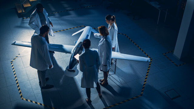 Meeting of Aerospace Engineers Work On Unmanned Aerial Vehicle Drone Prototype. Aviation Scientists in White Coats Talking. Industrial Laboratory with Surveillance or Military Aircraft. Elevated Shot