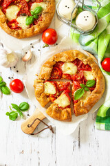 Healthy pastries made from rye flour, diet food. Galette tomatoes, mozzarella and basil on a wooden table. Top view flat lay background. Copy space.