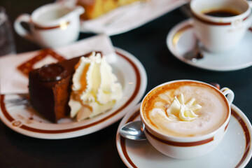 Coffee with cream in cap and with chocolate cake on table in cafe