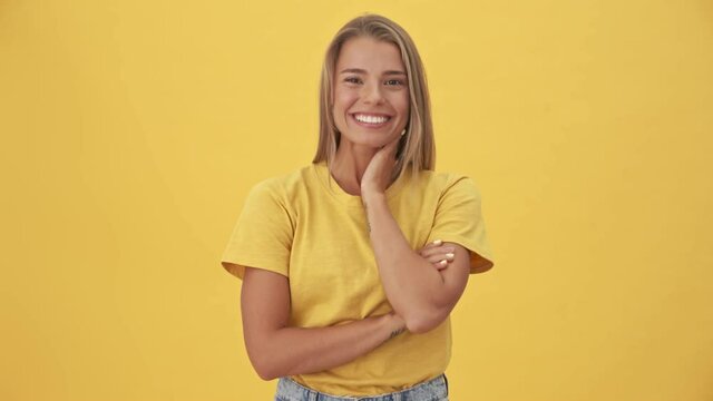 A beautiful young blonde woman in yellow T-shirt is laughing standing isolated over yellow background