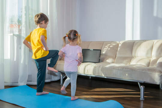 Preschooler boy and girl watching online video on laptop and doing fitness exercises. Kids sports at home, healthy lifestyle, stay at home, online learning, online training.