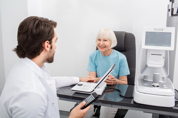 Smiling senior woman have consultation with her optometrist for an eye check-up. Eye exam and...