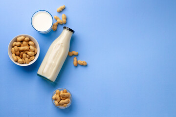 Peanut non dairy milk in glass bottle with bowl of peanuts on blue background