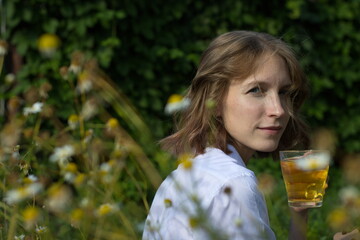 A young woman is drinking tea among the chamomile.