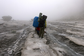 A tourists walks along the glacier. A tourist with a backpack and trekking poles is walking along the glacier. Glacier under the Koshtan pass (3513 meters above sea level). Caucasus.