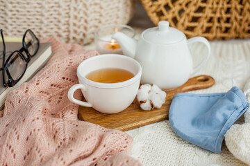 Laptop, face mask, hot tea mug, candle, glasses, kettle, wooden stand. Quarantine. Home Office. Cozy breakfast. Fall.