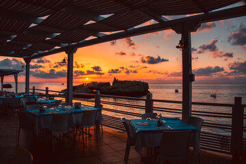 Sunset over water from the dining area of a sea front restaurant in southern Italy.Tables ready for service, silhouettes, amazing colored sky and sea.