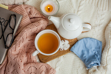 Laptop, face mask, hot tea mug, candle, glasses, kettle, wooden stand. Quarantine. Home Office. Cozy breakfast. Fall.