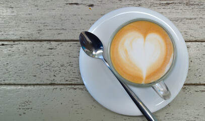 Hot coffee, cappuccino or heart-shaped latte in a glass on a wooden table.