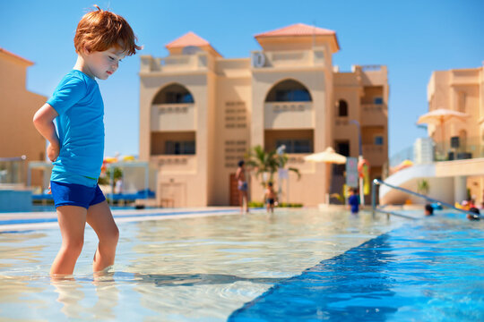 toddler boy in ultraviolet protective swimsuit walking in shallow water in the pool during summer vacation