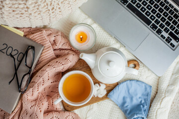 Laptop, face mask, hot tea mug, candle, glasses, kettle, wooden stand. Quarantine. Home Office. Cozy breakfast. Fall.