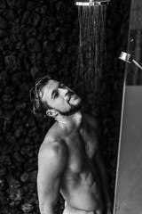 Topless handsome man taking a shower washing hair with shampoo product under water falling from...