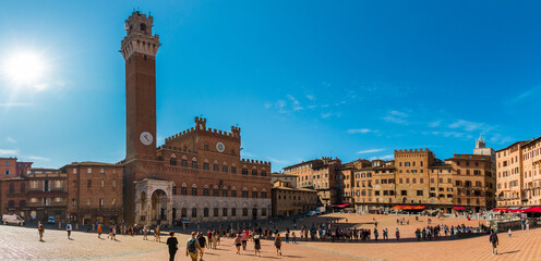 Obraz premium Malownicza panorama słynnego Palazzo Pubblico (ratusza) z dzwonnicą Torre del Mangia, na historycznym Piazza del Campo w słoneczny dzień z błękitnym niebem w Sienie, Toskania, Włochy.