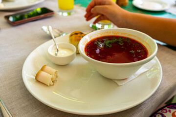 Beet soup in ceramic plate with becon, bread and sour cream on wooden board. Borch, traditional Ukrainian food