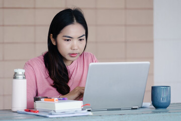 Young Asian freelance businesswoman working on a laptop at home during Coronavirus or COVID-19  pandemic. Young adult learner studying at home concept. Stock photo