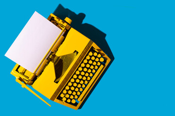 Yellow bright typewriter on blue. Symbol for writing, blogging, new ideas and creativity. Copy space - obrazy, fototapety, plakaty