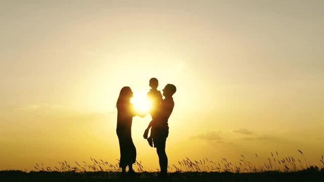 Silhouette of a happy family against a beautiful sunset. Father and mother hug and kiss their child. Emotions, kinship. teamwork
