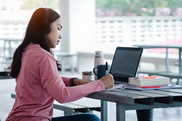 Fototapeta na wymiar Young Asian freelance businesswoman working on a laptop at home during Coronavirus or COVID-19 pandemic. Young adult learner studying at home concept. Stock photo