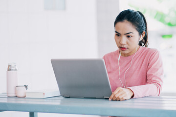 Young Asian freelance businesswoman working on a laptop at home during Coronavirus or COVID-19  pandemic. Young adult learner studying at home concept. Stock photo
