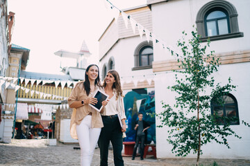 Cheerful Caucasian female tourists with modern touch pad exploring city urbanity satisfied with...