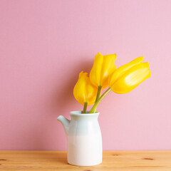 Yellow tulip flowers in vase on wooden table with pink background