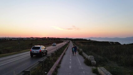 Slow motion view from above, stunning aerial drone view of a road that runs along a rocky coast bathed by sea in Sardinia, Italy with a senior couple walking - Powered by Adobe