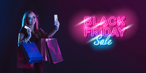 Online shopping. Portrait of young woman in neon on dark studio backgound. Human emotions, black...