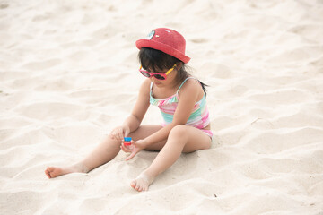 Happy asian child girl playing on white sand at the beach in summer. Asia kid girl with sunglasses and pink hat joyful on sand beach in thailand. people travel holiday concept. 