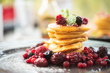 Delicious homemade pancakes with summer berries fruit for breakfast. Morning meal pancakes topped with honey on black dish.