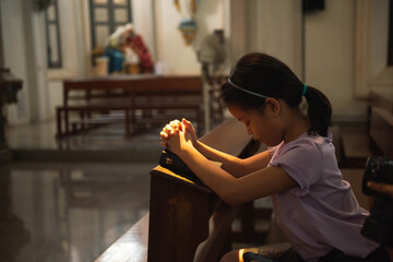Little asian girl with praying at christ church. Kid asia girl closed her eyes, praying to peace with scripture bible. people hope, dreams concept.