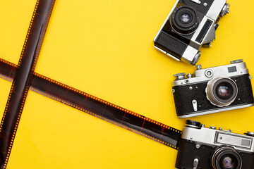 composition with three old cameras and film on a yellow background
