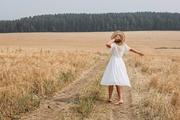 Fototapeta na wymiar A beautiful woman in a white dress and a straw hat walks in the field. 