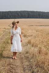 A beautiful woman in a white dress and a straw hat walks in the field. 