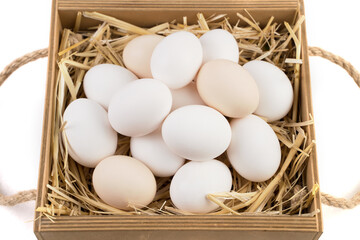 White and brown chicken eggs lie on straw in a wooden box. Side view. Food background. The concept of proper nutrition.