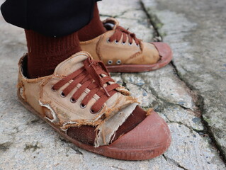 A boy in brown torn shoes is standing on a concrete floor.