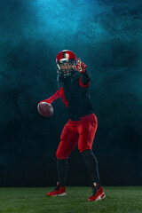 American football player, athlete sportsman in red helmet on dark background with smoke. Sport and...