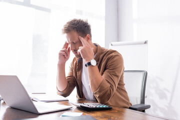 Selective focus of concentrated businessman sitting beside laptop and calculator on table in office