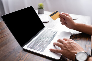 Cropped view of businessman using laptop and credit card at table in office