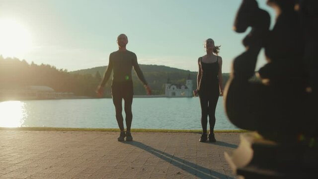 Close up man and woman doing exercise jum near lake at outdoor workout at sunlight sportswear active young sport runner fitness cardio summer slow motion
