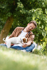 selective focus of young man playing with jack russell terrier dog while sitting on green grass