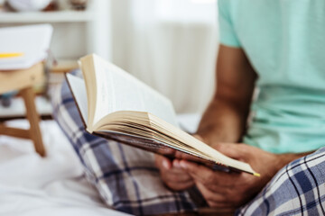 Close up photo of a young guy in pajamas while he reading a book.