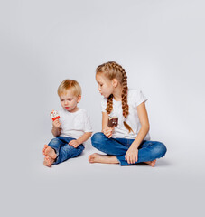 cute brother and sister in blue jeans and t-shirts eat ice cream