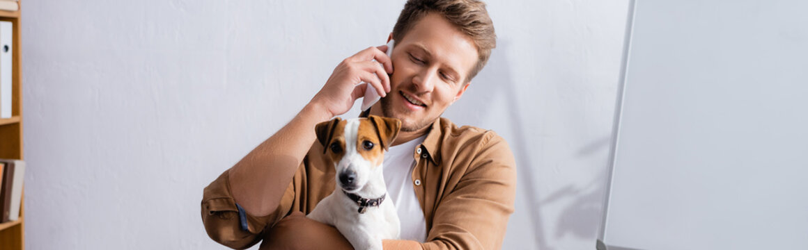 Horizontal Concept Of Businessman Talking On Mobile Phone And Holding Jack Russell Terrier Dog