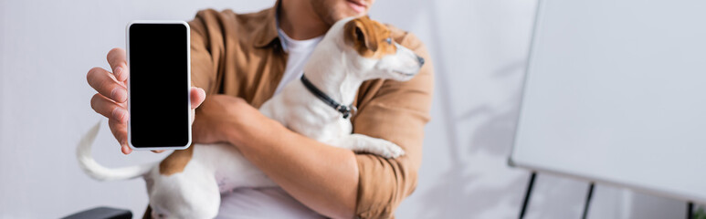 partial view of businessman showing smartphone with blank screen while holding jack russell terrier dog, panoramic shot